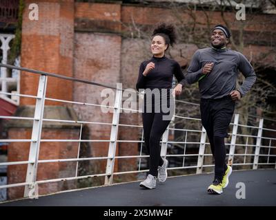 Lächelnder athletischer Mann und Frau, die auf dem Steg joggen Stockfoto