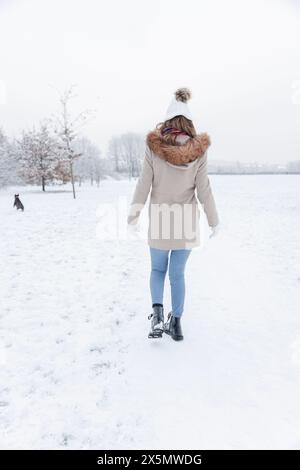 Rückansicht einer Frau, die mit Hund auf verschneiten Feldern läuft Stockfoto