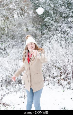 Lächelnde Frau, die Schneebälle in der Winterlandschaft wirft Stockfoto