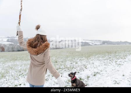 Rückansicht der Frau beim Wurfstock für Hund im verschneiten Feld Stockfoto