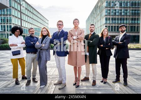 Geschäftsleute, die ihre Arme kreuzen, stehen vor Finanzgebäuden und blicken selbstbewusst in die Kamera. Stockfoto