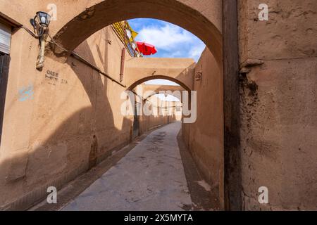 Alte Erdbögen säumen eine enge Gasse, über der nur ein roter Sonnenschirm steht. Traditionelle Architektur, Altstadt von Yazd, Iran. Stockfoto