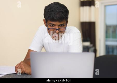 Ein entschlossener indischer Student sitzt an seinem Schreibtisch, vertieft in das Lernen auf seinem Laptop. Stockfoto