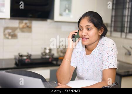Eine junge Frau konzentriert sich intensiv auf ihre Arbeit, während sie einen Laptop an ihrer Küchentheke benutzt. Stockfoto