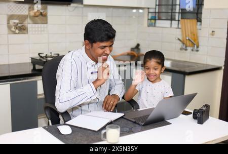 Dieses Bild handelt von einem indischen Vater und einer indischen Tochter, die einen Laptop in der Küche zu Hause benutzen Stockfoto
