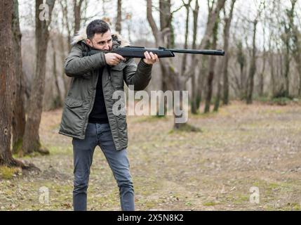 Junger Mann zielt und schießt mit Gewehr im Wald Stockfoto