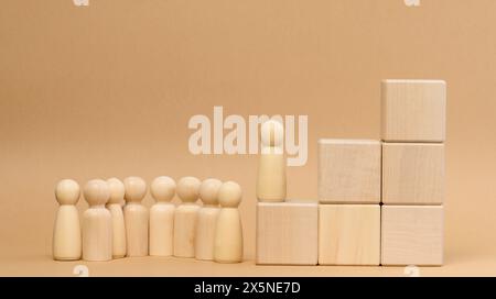 Holzfiguren von Männern auf einer Leiter aus Blöcken. Das Konzept des beruflichen Aufstiegs, Beginn am Arbeitsplatz, Erreichen von Zielen. Stockfoto