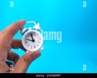 Hand mit weißem Wecker auf blauem Hintergrund und Kopierraum. Stockfoto