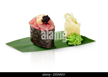 Thunfisch-Gunkan-Sushi mit Kaviar und Mayo, begleitet von Wasabi und eingelegtem Ingwer, präsentiert auf grünem Bambusblatt vor weißem Hintergrund. Trad Stockfoto