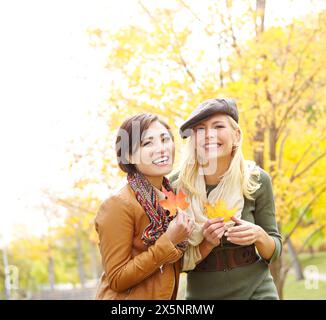 Die Magie des Herbstes teilen. Zwei attraktive Freundinnen halten Herbstlaub in ihrem Park. Stockfoto