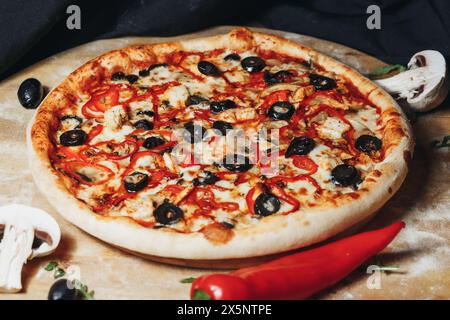 Frisch gebackene Peperoni und Oliven Pizza auf einem Holztisch umgeben von Zutaten Stockfoto