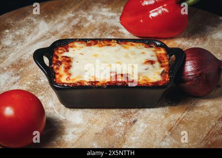 Gebackene Lasagne in einer schwarzen Keramikschale, umgeben von frischem Gemüse Stockfoto