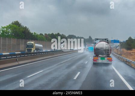 Lkw und andere Fahrzeuge, die an einem regnerischen Tag auf einer Autobahn fahren, verringern die Sicht aufgrund des Wassers, das von den Rädern aufgewirbelt wird. Stockfoto