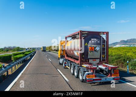 Lkw, der auf einer Autobahn mit einem Tankcontainer mit Etiketten und Gefahrenschildern für giftige Flüssigkeiten nach dem internationalen abkommen über gefährliche Go fährt Stockfoto