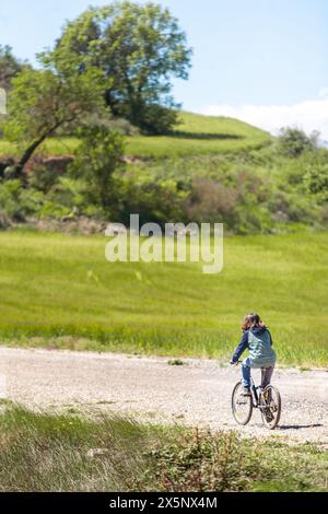 Ein kleiner Junge fährt mit dem Fahrrad auf einer Feldstraße auf einem grasbewachsenen Feld. Die Szene ist friedlich und ruhig, der Junge genießt die frische Luft und die Schönheit o Stockfoto