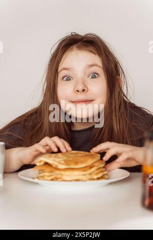 Kleines, fröhliches Teenager-Mädchen, das sich bereit macht, einen Stapel Pfannkuchen zu essen. Hochwertige Fotos Stockfoto