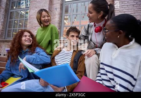 Gruppe glückliche Studenten, die auf der Bank sitzen, sammelten das Lernen mit Arbeitsbüchern auf dem Universitätscampus Stockfoto