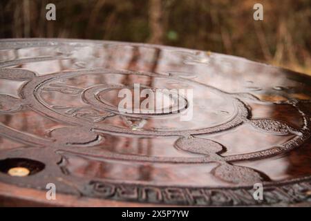 Nahaufnahme eines Mannlochdeckels mit Regenwasser darauf Stockfoto