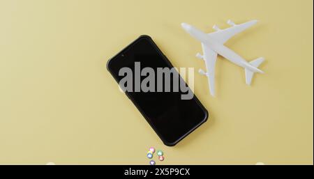 Smartphone in der Nähe von weißem Flugzeugmodell mit bunten Pillen auf gelbem Hintergrund Stockfoto