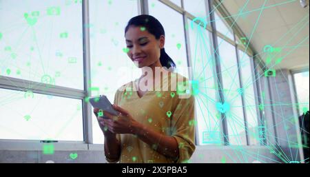 Bild von verbundenen Symbolen, die Kugeln über asiatischen Frauen bilden, die auf dem Smartphone scrollen Stockfoto