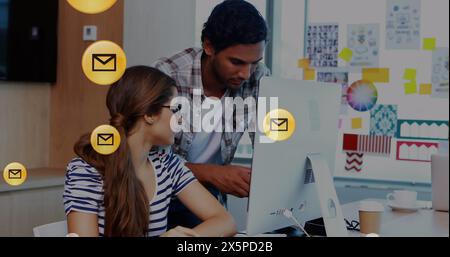 Bild von sich bewegenden Umschlägen im Kreis über verschiedene Mitarbeiter, die über Desktop-PCs im Büro planen Stockfoto
