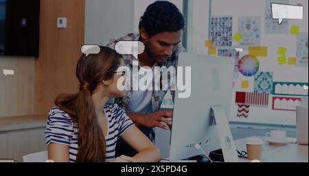 Bild von schwankenden Sprachblasen über multirassischen Kollegen, die im Büro über Desktop diskutieren Stockfoto