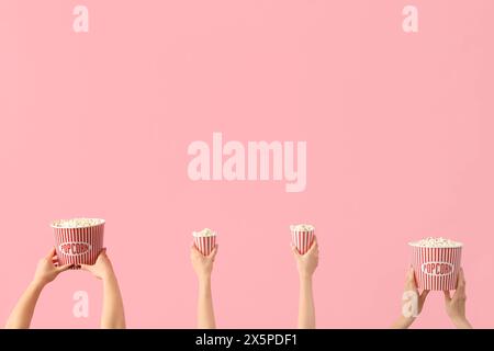 Hände halten Eimer mit Popcorn auf rosa Hintergrund Stockfoto