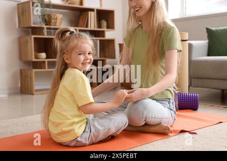 Junge sportliche Frau mit ihrer kleinen Tochter, die zu Hause Yoga praktiziert Stockfoto