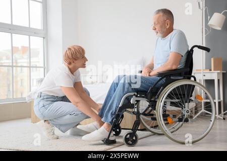 Reife Frau hilft ihrem kranken Ehemann im Rollstuhl zu Hause Stockfoto