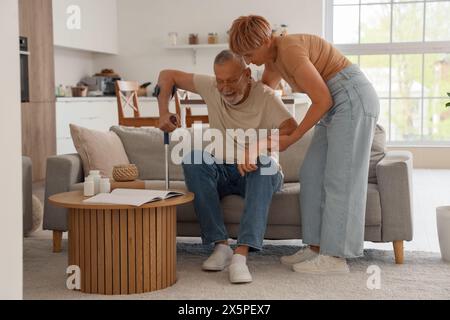 Reife Frau hilft ihrem Mann mit Krücken, zu Hause vom Sofa aufzustehen Stockfoto