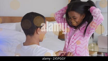 Bild des Lichts, das sich über eine glückliche afroamerikanische Mutter und Tochter bewegt, die Pyjama anziehen Stockfoto