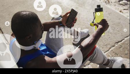 Bild von Profilsymbolen über müden afroamerikanischen Athleten, die sitzen und auf das Smartphone schauen Stockfoto