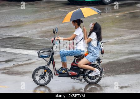 SAMUT PRAKAN, THAILAND, 20. März 2024, zwei Frauen mit Regenschirmen fahren im Regen mit einem Elektrofahrrad Stockfoto