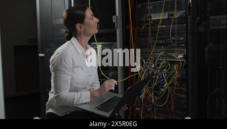 Kaukasierin, die einen Laptop hält, im Serverraum arbeitet Stockfoto