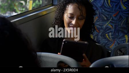 Birassische Frau, die ein Tablet im Bus hält und auf den Bildschirm blickt Stockfoto