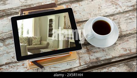 Tablet mit gemütlichem Wohnzimmer, das neben einer Kaffeetasse auf Notebooks liegt Stockfoto