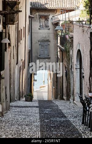 Enge Kopfsteinpflasterstraße zwischen alten Gebäuden, die in Richtung eines Sees in einer malerischen alten italienischen Stadt führt Stockfoto