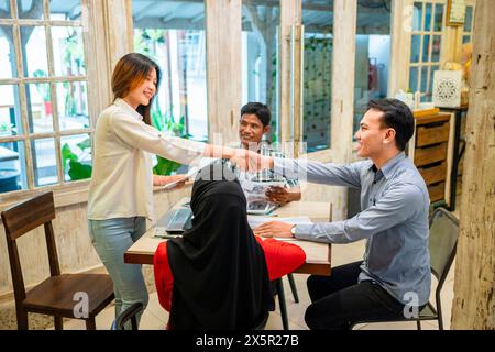 Indonesischer Büroangestellter Handschlag mit weiblicher Mandantin bei einem Meeting in einem modernen Start-up-Unternehmen am Arbeitsplatz. Diversität professionelles Teamkonzept. Stockfoto