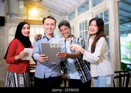 Multiethnische Geschäftsleute lächeln zu einem Meeting in einem Café oder Restaurant und zeigen ein digitales Tablet. Gruppe junger indonesischer Unternehmer, die arbeiten Stockfoto