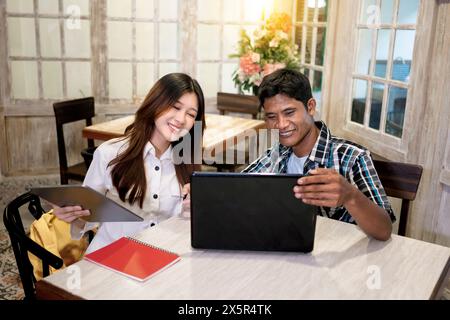 Zwei glückliche junge Diversity-Geschäftsleute, die einen Videoanruf in einem Café machen. Zwei indonesische, fröhliche Unternehmer, die zusammen arbeiten und online teilnehmen, treffen sich Stockfoto