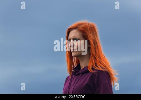 Porträt einer rothaarigen nachdenklichen jungen Frau vor blauer Wolke Stockfoto