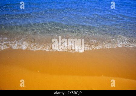 Sanfte Wellen, die in einer Nahaufnahme über goldenen Sand unter klarem blauen Himmel schweben Stockfoto
