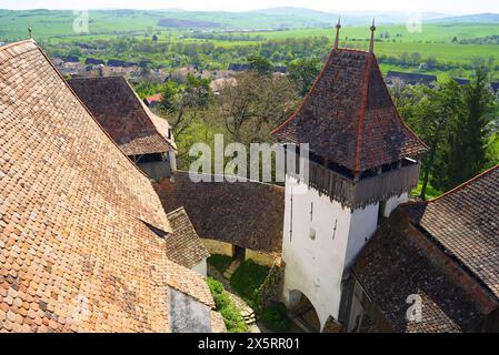 Landschaft vom Glockenturm der Kirche in Viscri: Alte Ziegeldächer, Verteidigungsmauern, ein Turm und hinter einem Blick auf das Dorf umgeben von Feldern Stockfoto
