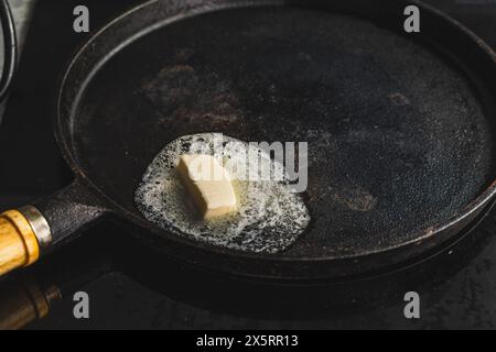 Ein Stück Butter wird in einer gusseisernen Pfanne geschmolzen. Der Anfang des Kochens. Hochwertige Fotos Stockfoto