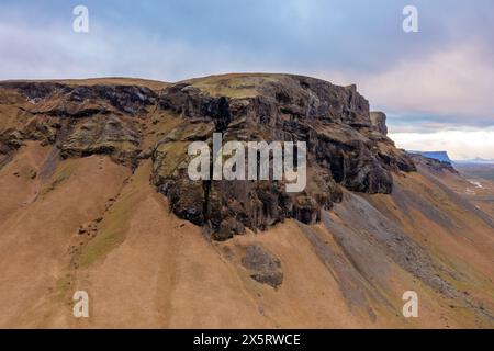 Aus der Vogelperspektive hoher Berg im Osten Islands. Hohe Felsen bedeckt mit Moos. Blaugrauer, bewölkter Himmel Stockfoto