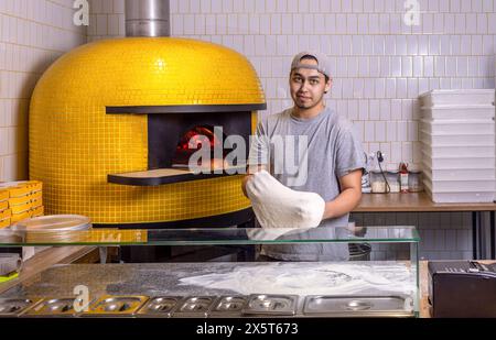 Koch bereitet Pizzateig zu. Der Prozess der Pizza. Ein erfahrener Koch bereitet Teig für Pizza zu, die mit den Händen gerollt wird, während er in einem Pizzeria arbeitet. Die Stockfoto