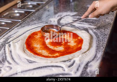 Nahaufnahme Hand von Koch Bäcker, der Pizza in der Küche macht. Der Prozess der Zubereitung von Pizza. Der Koch gießt Tomatensauce über den gerollten Teig. Küchenchef Hand ist Stockfoto