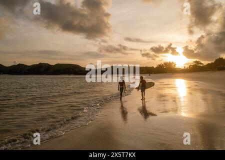 Indonesien, Lombok, Silhouette der Surfer, die bei Sonnenuntergang am Strand spazieren Stockfoto