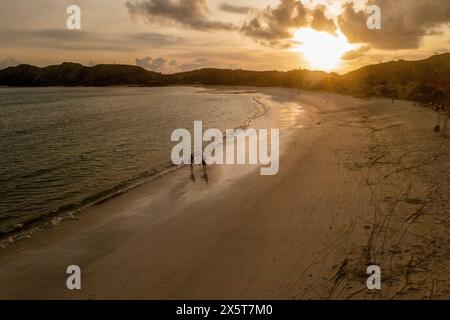 Indonesien, Lombok, aus der Vogelperspektive auf Surfer, die bei Sonnenuntergang am Strand spazieren Stockfoto