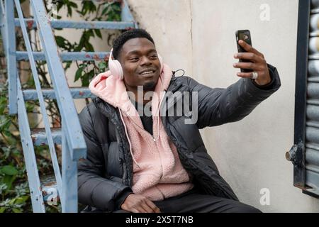 Junger Mann, der auf der Treppe sitzt und Selfie macht Stockfoto